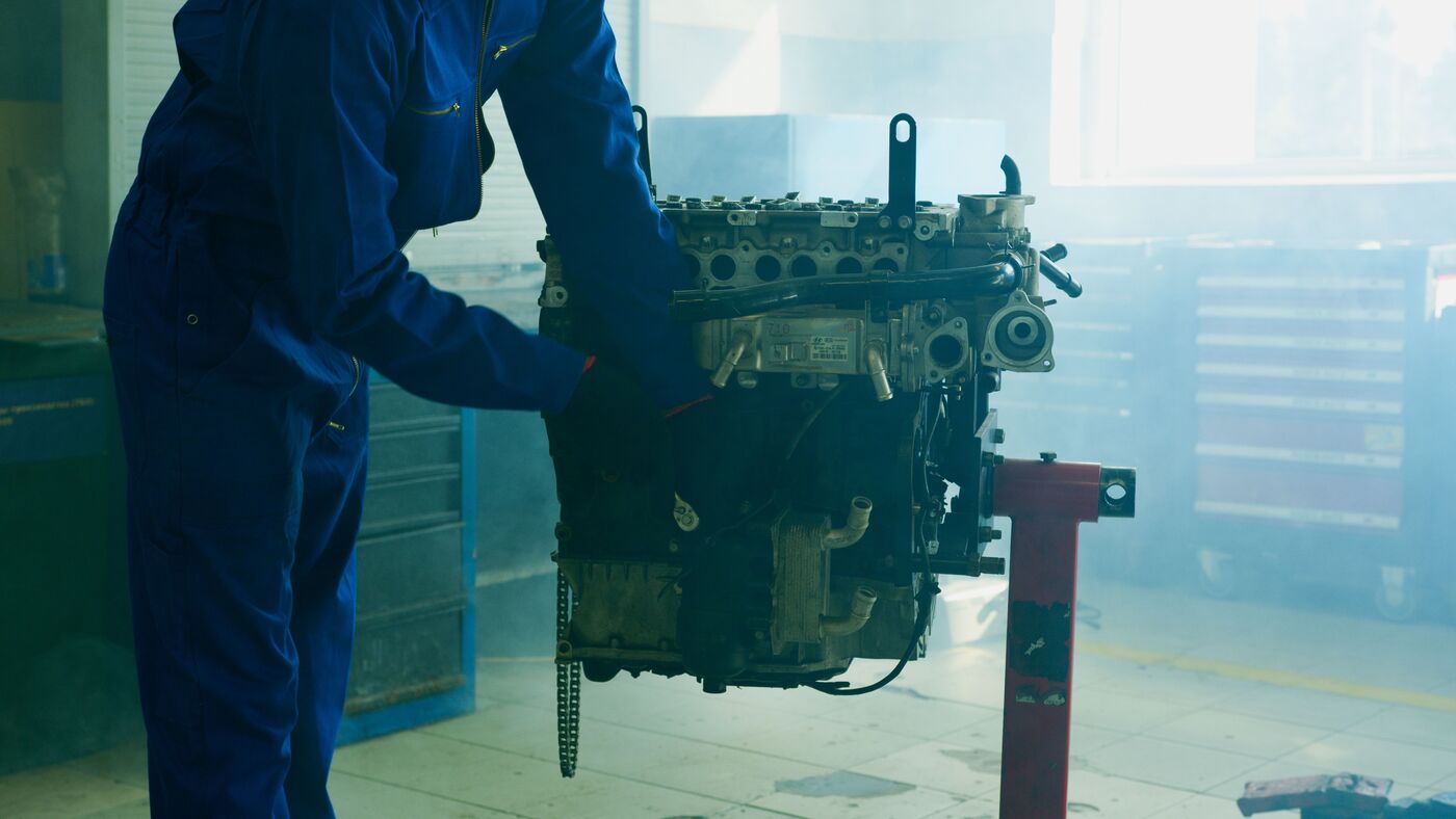 A technician in overalls examining a car engine mounted on a workshop stand