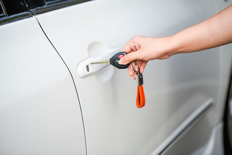 A hand holding a car key beside the door handle of a locked car