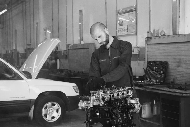A mechanic in overalls working on a stripped-down engine at a workshop bench